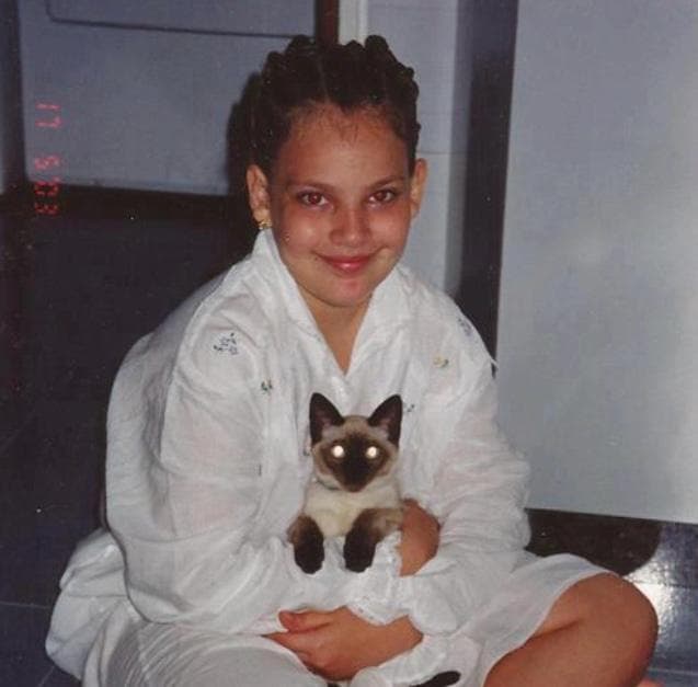 Oriana de niña sosteniendo un gatito siamés — una vocación que empezó desde temprano